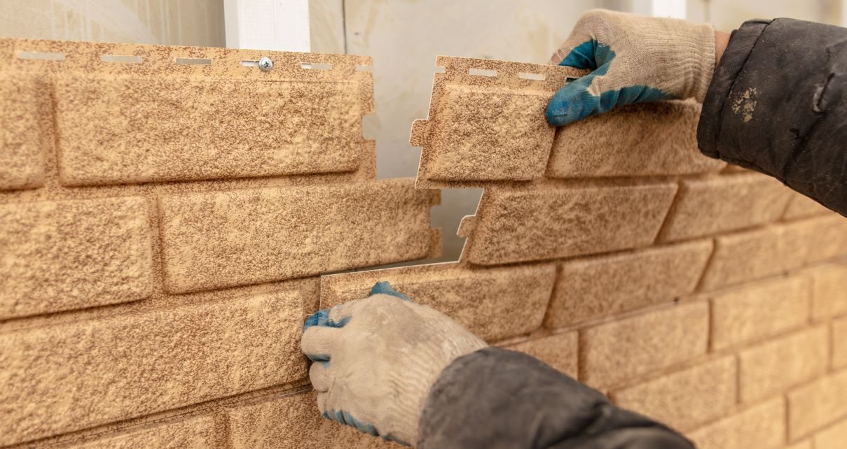 A construction worker installs vinyl siding that looks like brick.