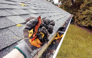A gloved hand cleans leaves out of a home's rain gutter.
