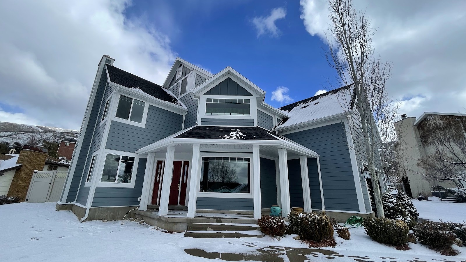 A two-story blue house with white trim and a covered porch sits in a snowy yard under a partly cloudy sky, showcasing durable James Hardie siding—an ideal choice for Utah homes. A two-story blue house with white trim and a covered porch sits in a snowy yard under a partly cloudy sky, showcasing durable James Hardie siding—an ideal choice for Utah homes.