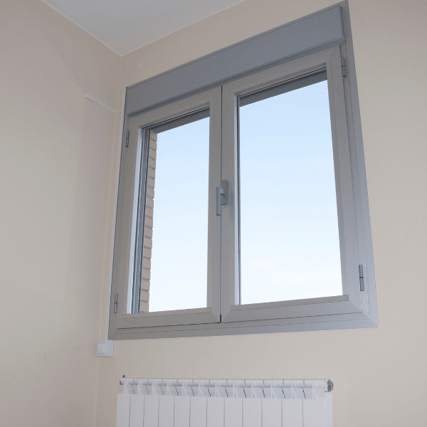A closed, modern aluminum double-pane window with a grey frame, set in a beige wall above a white radiator, showcases expert window installation in Salt Lake City, Utah, with a clear sky visible outside. A closed, modern aluminum double-pane window with a grey frame, set in a beige wall above a white radiator, showcases expert window installation in Salt Lake City, Utah, with a clear sky visible outside.