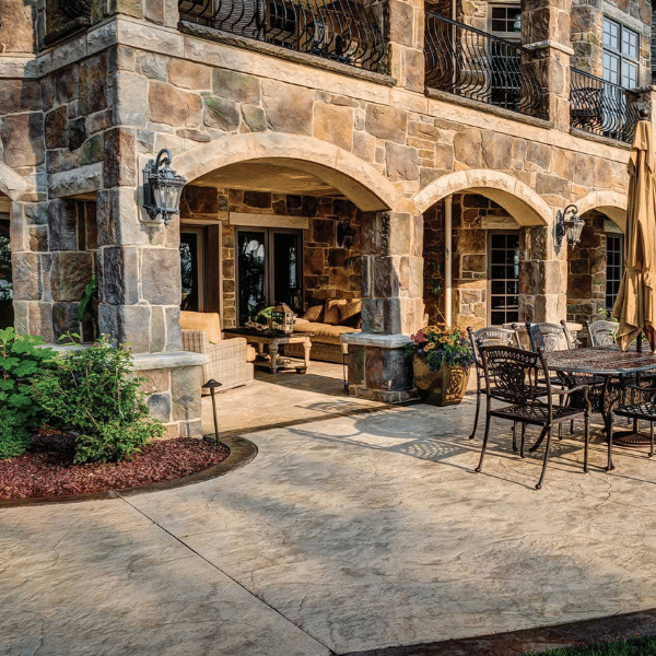 Stone patio area with arched columns, outdoor seating, dining table, chairs, potted plants, and umbrella enhance the charm of this large stone house featuring Casa di Sassi stone veneer installation. Stone patio area with arched columns, outdoor seating, dining table, chairs, potted plants, and umbrella enhance the charm of this large stone house featuring Casa di Sassi stone veneer installation.