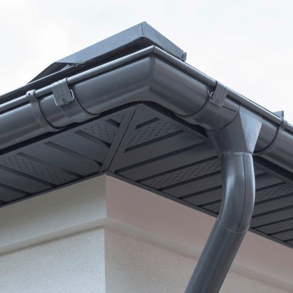 Close-up of a house corner in Salt Lake City showing a black rain gutter system with a downspout attached to the roof, vented eaves, and white exterior walls—perfect for showcasing quality gutter installation. Close-up of a house corner in Salt Lake City showing a black rain gutter system with a downspout attached to the roof, vented eaves, and white exterior walls—perfect for showcasing quality gutter installation.