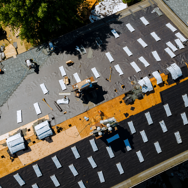 Aerial view of a building roof under construction in Salt Lake City, with tools, materials, and partially installed roofing layers showcasing the roofing installation process. Aerial view of a building roof under construction in Salt Lake City, with tools, materials, and partially installed roofing layers showcasing the roofing installation process.