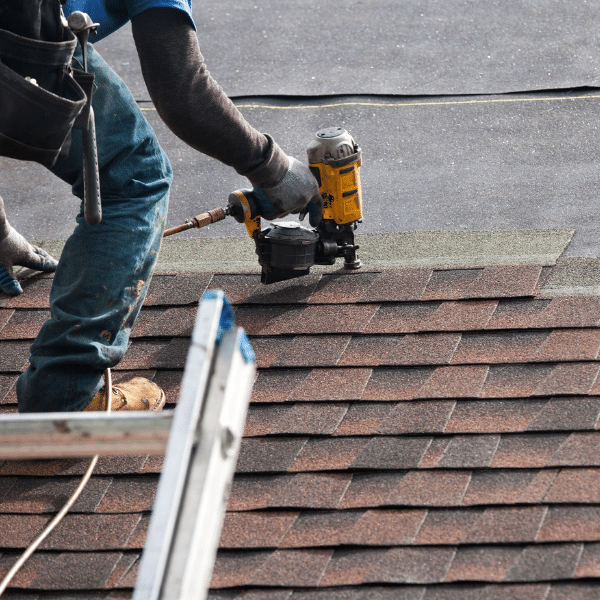Person using a nail gun to install asphalt shingles on a roof during a roofing installation in Salt Lake City, Utah, with a ladder in the foreground and work tools visible. Person using a nail gun to install asphalt shingles on a roof during a roofing installation in Salt Lake City, Utah, with a ladder in the foreground and work tools visible.