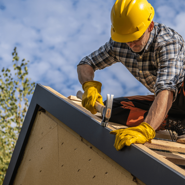 A construction worker in a yellow hard hat and gloves uses a hammer for roofing installation on a building in Salt Lake City, Utah, under a partly cloudy sky. A construction worker in a yellow hard hat and gloves uses a hammer for roofing installation on a building in Salt Lake City, Utah, under a partly cloudy sky.