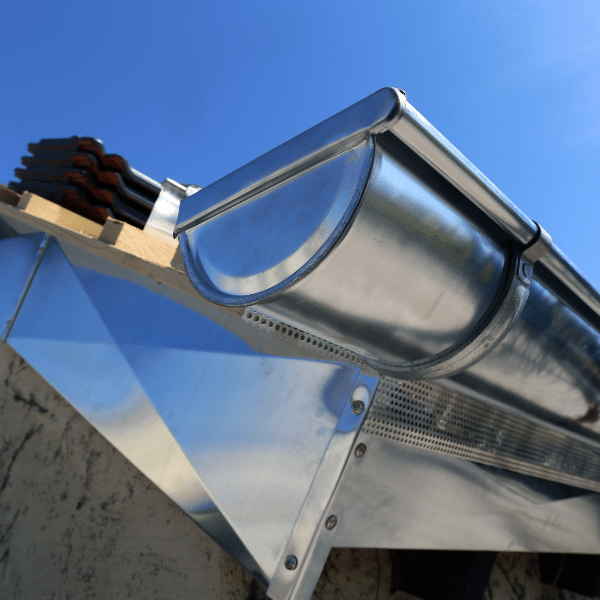 Close-up of a shiny steel gutter installation along the edge of a roof under a clear blue Salt Lake City sky. Close-up of a shiny steel gutter installation along the edge of a roof under a clear blue Salt Lake City sky.