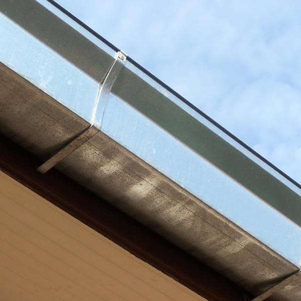 A close-up view of a steel gutter installation attached to the edge of a roof in Salt Lake City, Utah, with a blue sky and some clouds in the background. A close-up view of a steel gutter installation attached to the edge of a roof in Salt Lake City, Utah, with a blue sky and some clouds in the background.