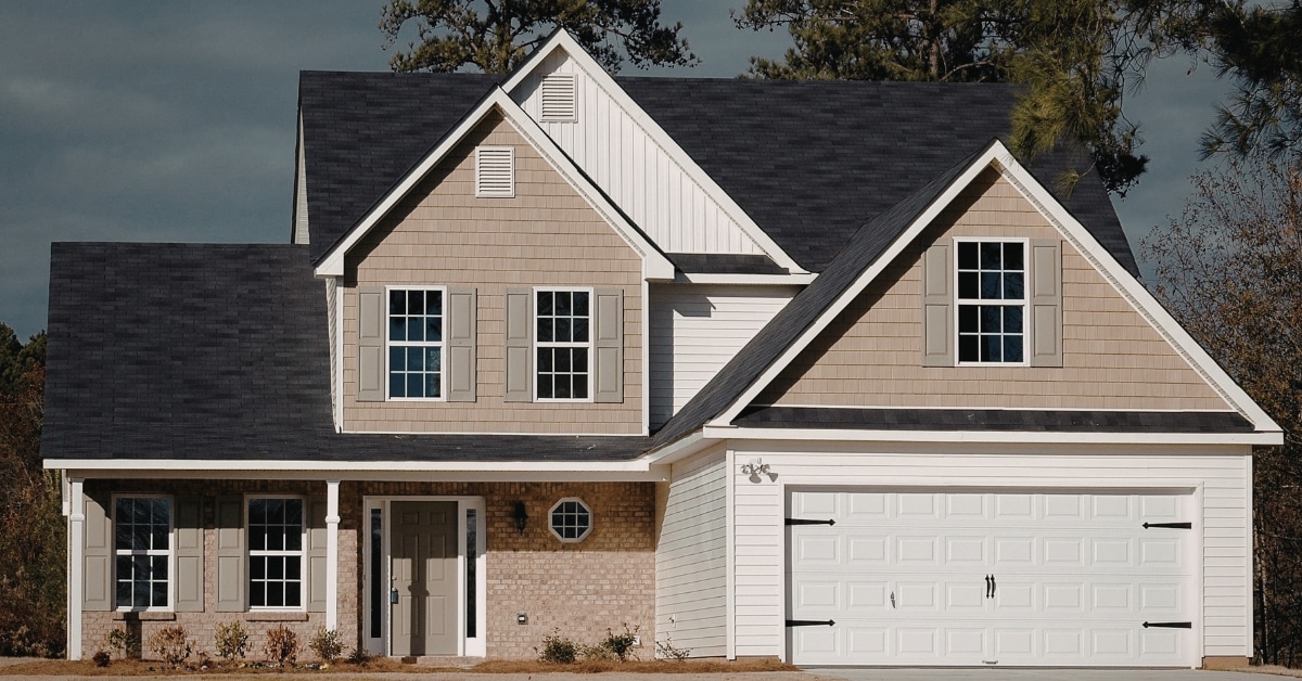 Two-story suburban Utah house with beige brick and siding, dark roof, white trim, front door, and a double garage, photographed during the day. Two-story suburban Utah house with beige brick and siding, dark roof, white trim, front door, and a double garage, photographed during the day.