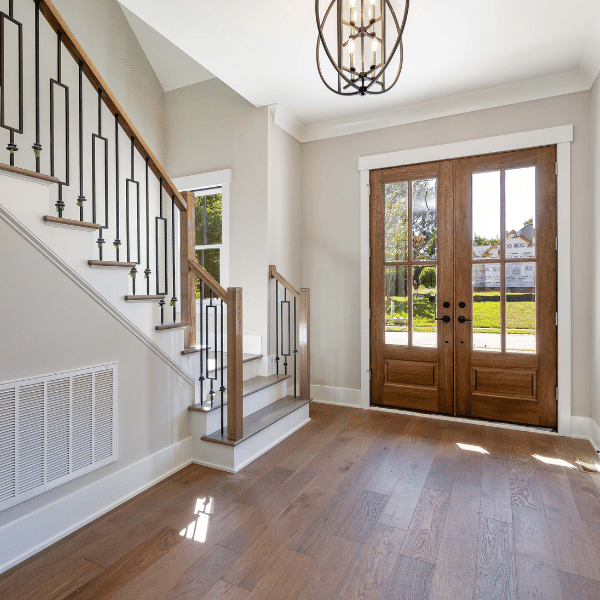 A bright entryway with wooden double doors, hardwood flooring, a staircase with black railings, and a modern light fixture. Sunlight streams through the doors and windows, filling the space with warmth. A bright entryway with wooden double doors, hardwood flooring, a staircase with black railings, and a modern light fixture. Sunlight streams through the doors and windows, filling the space with warmth.